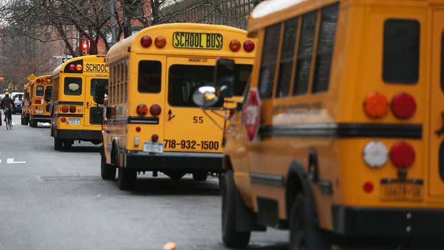 A photo of five New York city school buses parked in a line. 