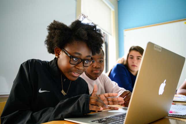 An image from Girls Who Code depicting three young people sitting in front of a macbook, probably coding.