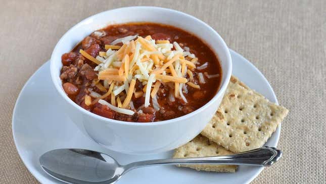 Bowl of chili with cheese on top beside spoon and crackers