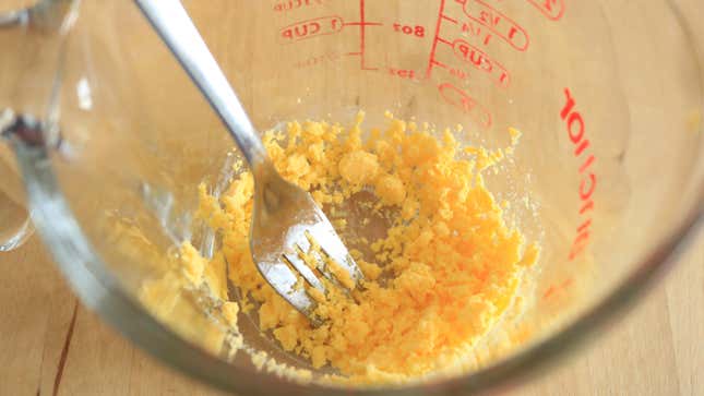 Cooked egg yolk broken into a measuring cup with a fork.