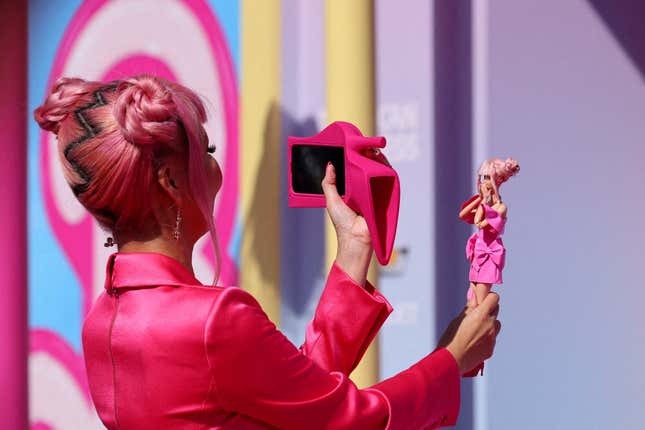 A fan with two pink buns and wearing a pink top takes a photo of a Barbie doll at the world premiere of the film "Barbie" in Los Angeles