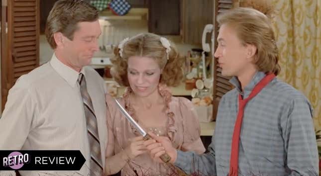 A woman in a pink dress stands between two men, the younger of whom is wearing a red tie and pointing a knife at the older man.