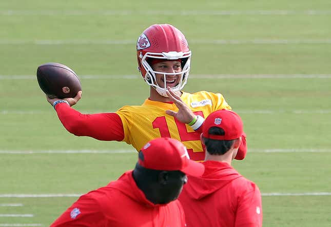 A man in a red football helmet and a yellow practice jersey cocks his arm and prepares to throw a football.