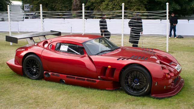 A red TVR Cerbera Speed 12 is parked on grass.