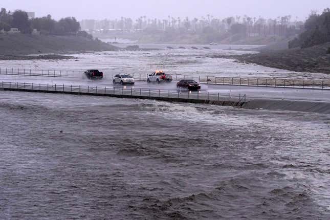 Vehicles cross over a flood control basin that has almost reached the street, on Sunday, August. 20, 2023, in Palm Desert, California. 