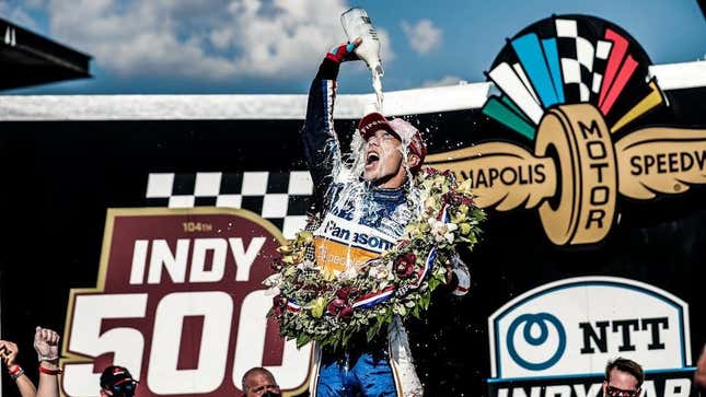 Japanese driver Takuma Sato celebrates his second victory at the 2020 Indianapolis Motor Speedway. He is pouring milk over his head while wearing the traditional winner's wreath.