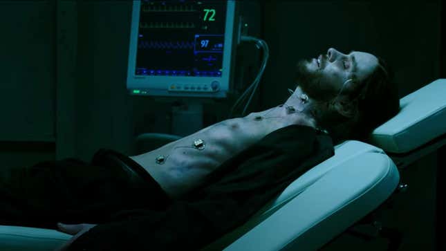 Morbius, looking pale and sickly, lies shirtless on a hospital bed next to a heart rate monitor.