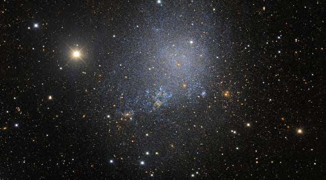An irregular dwarf galaxy is a smattering of blue and orange stars.