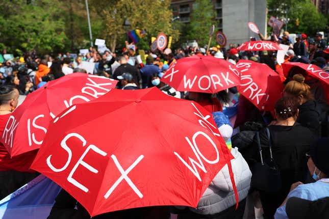 People participate in a May Day rally in Washington Square Park holding red umbrellas that read "sex work is work!"