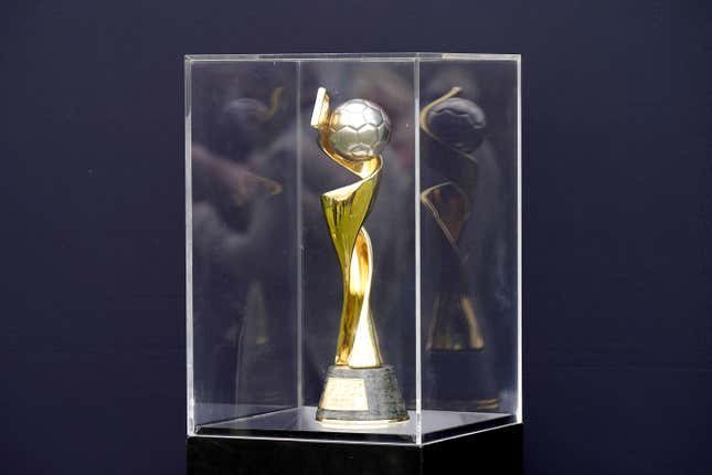 A trophy made up of a silver soccer ball atop a golden swirl sits inside a plexiglass box before a black background.
