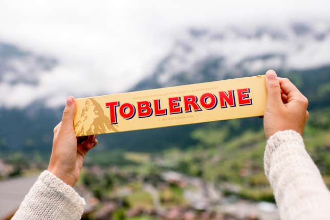 Una persona sosteniendo una tableta de chocolate Toblerone frente a las montañas suizas.