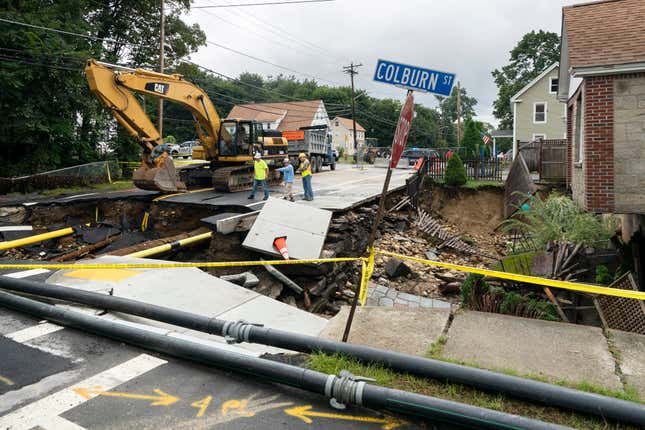 Funcionarios de obras públicas examinan los daños a una carretera y un patio delantero que fueron arrasados   por una inundación reciente el 13 de septiembre de 2023 en Leominster, Massachusetts. 