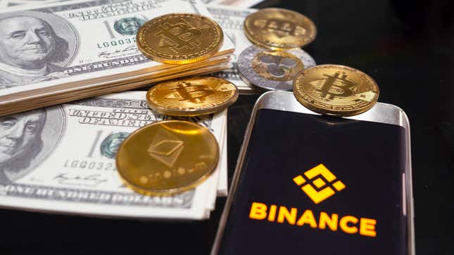 Mobile phone with on screen logo of binance surrounded by 100 dollar bills and golden crypto and ethereum coins.