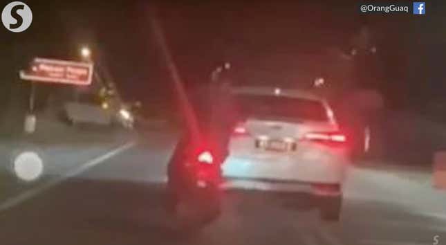 The blurry back of a Toyota Vios on a dark road in Malaysia. A motor bike follows close behind. 