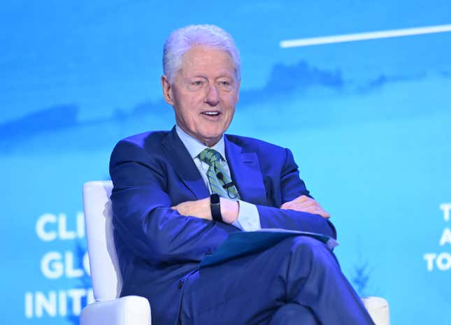 Former US president Bill Clinton sits with his arms folded.