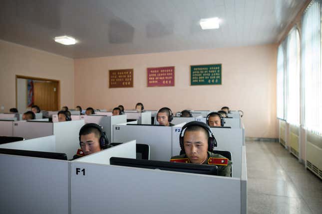 Several young men in army uniforms and headphones sit behind computers in cubicles.