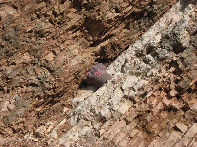 Rocks near Gubbio, Italy, change in color and texture at the line indicating the Cretaceous-Paleogene extinction event that wiped out the dinosaurs 66 million years ago. A baseball hat shows scale.
