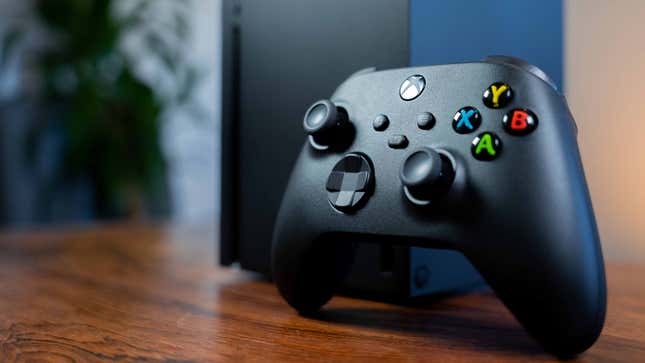 An Xbox Series X controller rests against an Xbox Series X on a table.