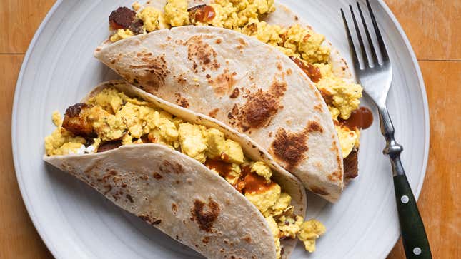 Top-down photo of two breakfast tacos in flour tortillas on a white plate. 