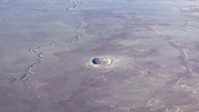 A bowl-shaped crater at center is the main detail on the otherwise flat, red-grey Arizona terrain.