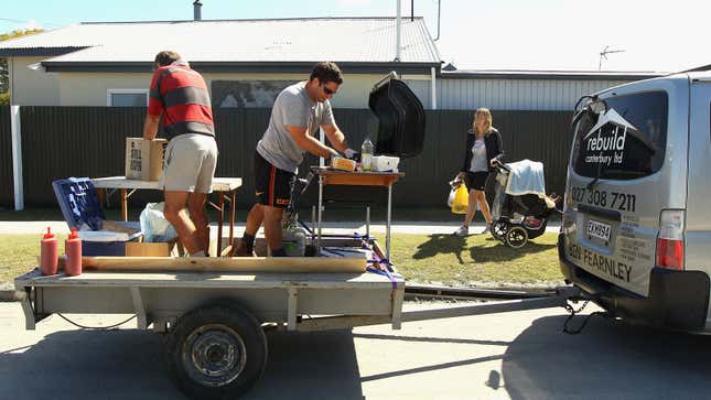 Two people serve BBQ from the back of a trailer. 