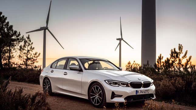 A photo of a BMW 330e sedan with wind turbines in the background.