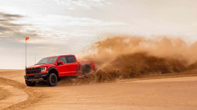 A photo of a red Ford F-150 Raptor pickup truck driving on sand. 