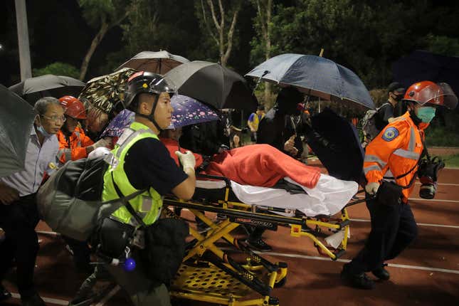Medics transport an injured student under the cover of umbrellas.