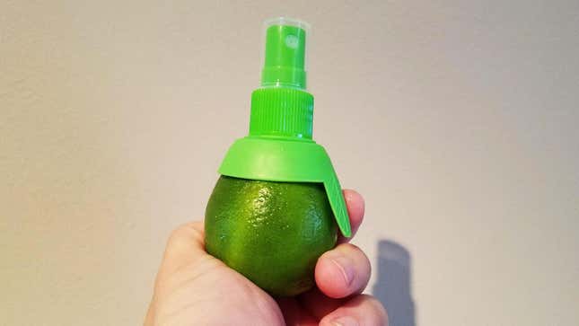 Hand holding up a lime with a citrus sprayer screwed into it