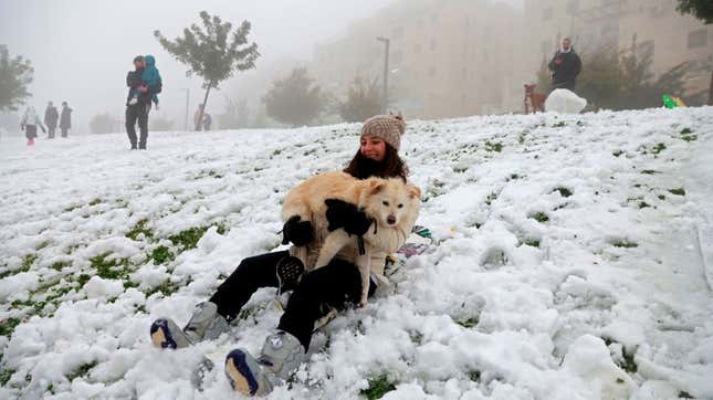 A woman holding a dog slides down a snow-covered slope following a snowstorm in Jerusalem, on Feb. 18, 2021.