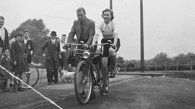 A black and white photo of two people riding a Sociable bike. 