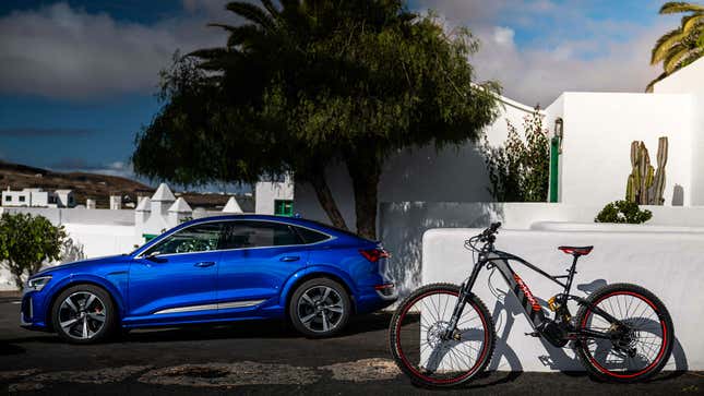 A photo of a grey Audi e-bike next to a blue electric car. 