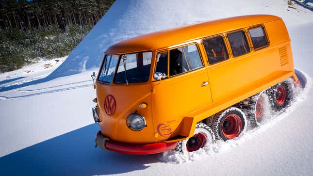 A photo of an orange VW bus with tank tracks on its rear wheels. 