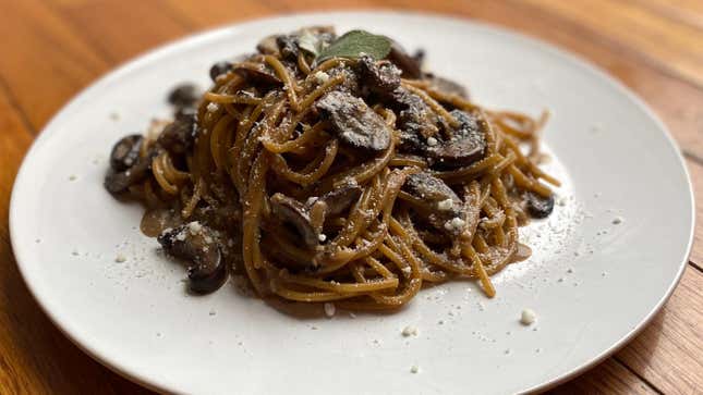White plate with spaghetti, mushrooms, and Parmesan