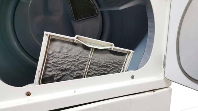 A dryer lint trap full of lint pokes out of the slot in an open dryer