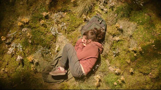 Bella Ramsey as Ellie sleeps curled up in a grassy space in HBO's The Last of Us.