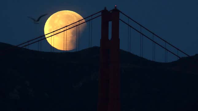 A photo of the Golden Gate Bridge at night time with the full moon behind. 