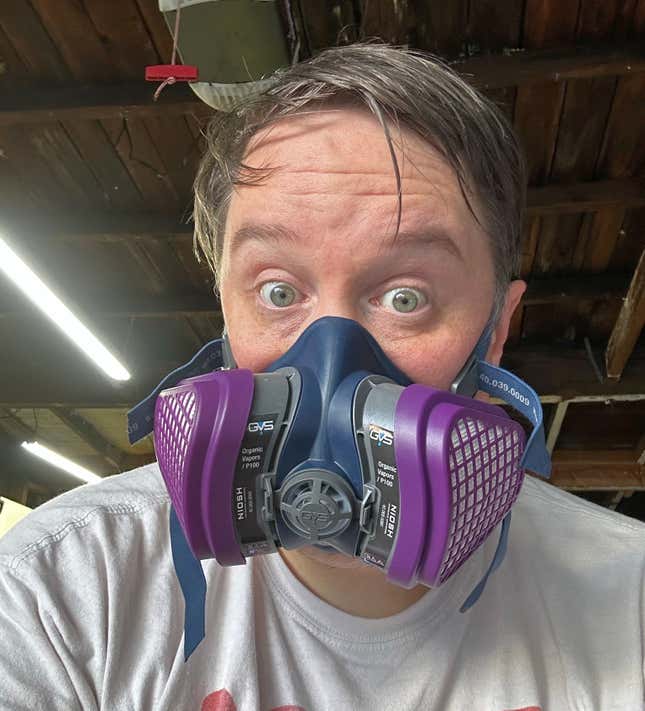 A surprised looking man with brown hair is wearing a purple and blue respirator.