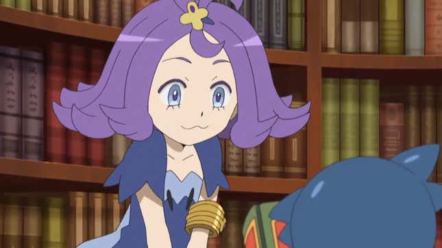 Acerola is seen standing in front of a large shelf of books.
