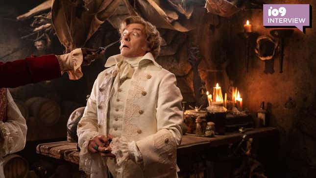 Pirate Stede Bonnet, wearing a fancy white outfit, is menaced by a dagger close to his eye.