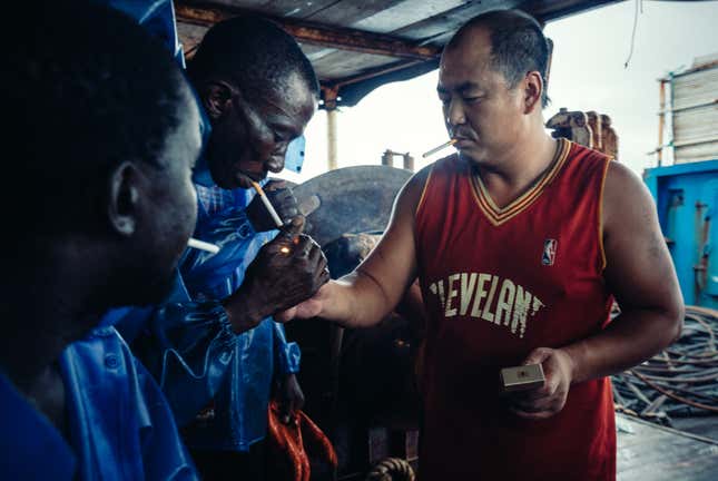 Chief mate Wang of a boat in the Atlantic naval territory of Guinea-Bissau passes cigarettes to local sailors.