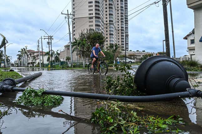 A man cycles through water past a downed street lamp in the aftermath of Hurricane Ian in Fort Myers, Florida, on September 29, 2022. 