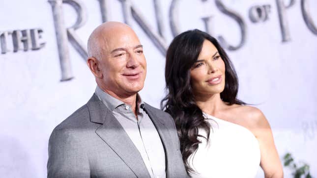Jeff Bezos stands next to TV personality Lauren Sanchez in front of a poster for Amazon Prime Video's The Lord of the Rings The Rings of Power