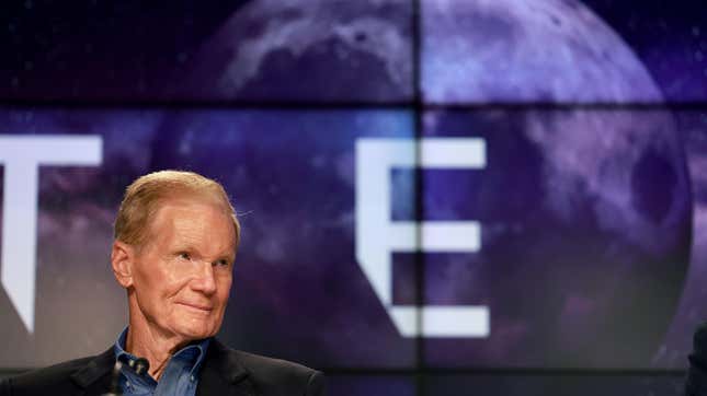 Bill Nelson looks to the side in front of a screen showing the moon.