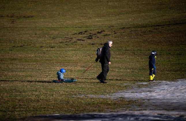 A man pulls a child in a sled over grass in Filzmoos, Austria.
