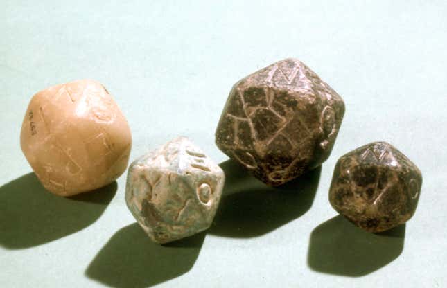 Four well-worn, multi-sided die sit next to each other on a white table.