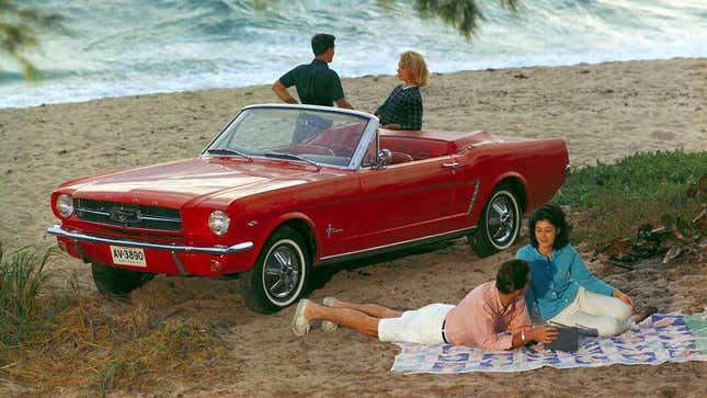 People hanging out around a 1964 Ford Mustang on the beach. 