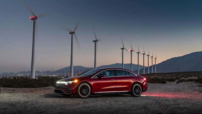 A photo of a red Mercedes EQS Sedan parked in a wind farm. 