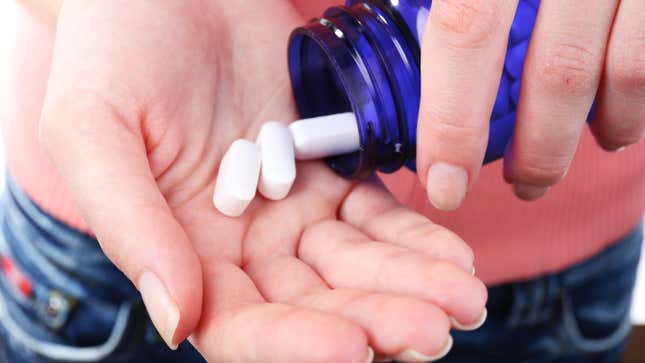 A woman pours three small white tablets from a blue glass bottle into her hand