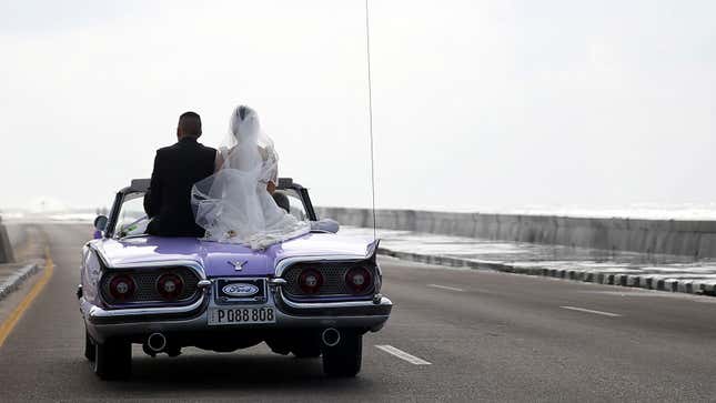 A bride and groom ride in a convertible classic Ford. 